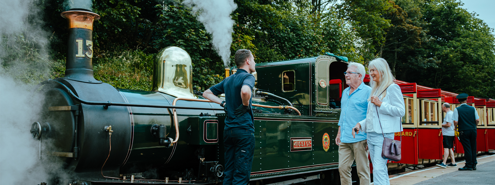 A couple standing next to the Steam Railway on the Isle of Man talking to the Railway driver